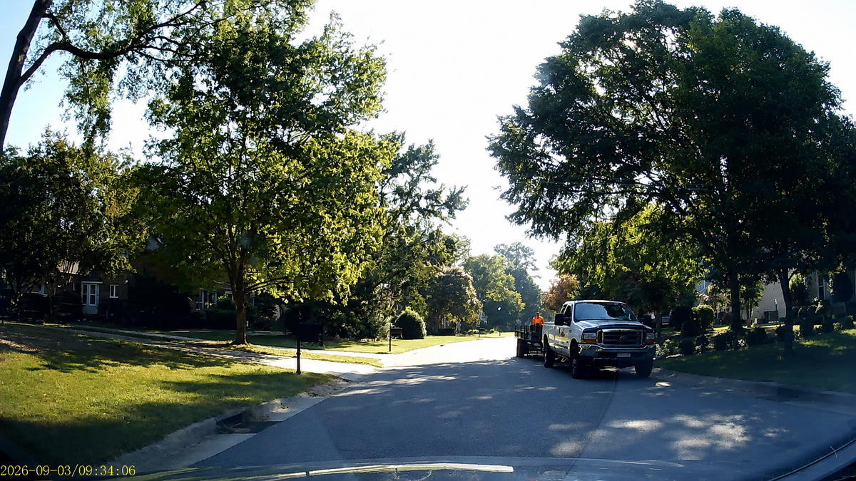 Dash cam still frame of a sunny neighborhood street with a pickup truck ahead and timestamp overlay